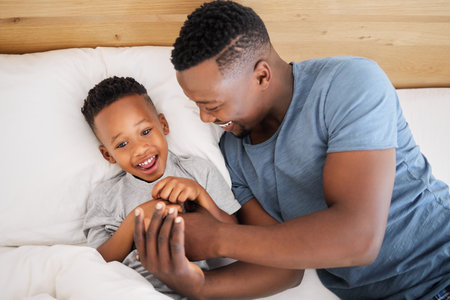 Father, son and happy in bed or home for bonding, relaxing and smile for relationship together in bedroom. Weekend, black man and care on holiday in apartment for childhood, parent and morningの写真素材