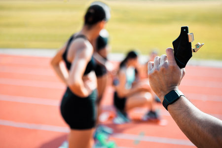 Hand, race and fire starter gun for running or exercise with athlete on track. Starting pistol, group or women at stadium field to get ready for training, cardio or sprint competition closeup outdoorの写真素材