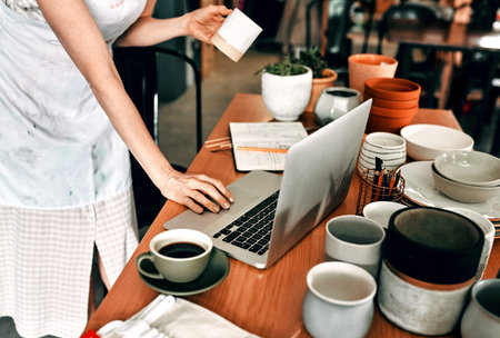 Woman, hands and laptop in pottery workshop for check website inventory, startup and art store....