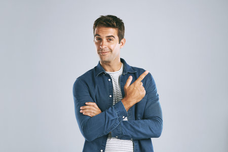 Portrait, pointing and man with review, option and model on grey studio background. Face, person and guy with hand gesture, mockup space and promotion with discount deal, information and opportunityの写真素材