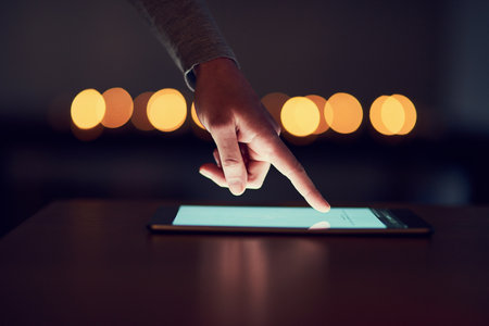 Hand, screen and smartphone on table at night for social media, communication or networking. Bokeh, closeup and person with mobile for browsing internet, trending update or notification in homeの写真素材