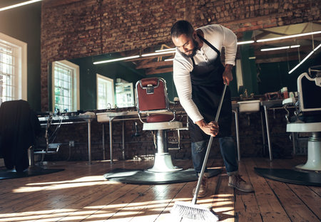 Barber, salon and man with broom for cleaning after grooming, shaving and hair cut for beauty...