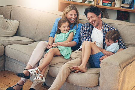 Family, relax and parents with children, funny and joke by dad, comedy and couch in house. Home, woman and man with kids, together and bonding for break in apartment, laughing and mom with loveの写真素材