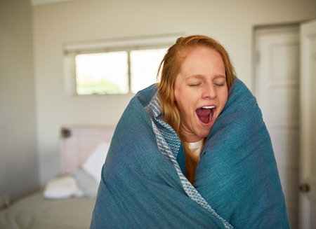 Woman, blanket and tired in morning with yawn for burnout, warm and sleeping problem in home. Female...