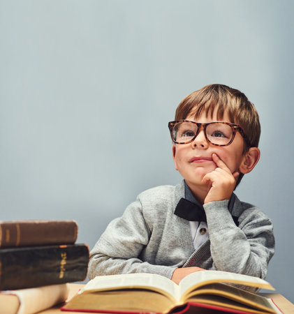 Boy, child and books in studio for learning, glasses and education with mock up space by blue background. Kid, textbook and vision for future with studying, scholarship and development at academyの写真素材