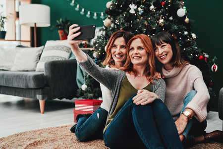 Selfie, sisters or women in home for Christmas celebration with relax together and social media post for family. Female people, smile and group of friends for holiday party or video call with contactの写真素材