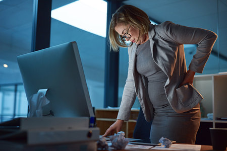 Business woman, back injury and night with pain for accident, strain or overworked at office. Frustrated female person, employee or sore spine in ache or muscle tension from working late at workplaceの写真素材
