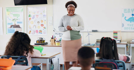Teacher, children and talking in classroom for lesson, advice or smile with assessment for development. Woman, child and quiz for education, info or knowledge for help, happy or scholarship at schoolの写真素材
