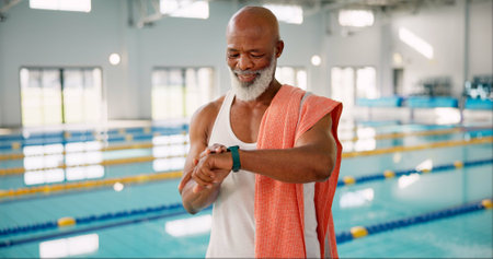 Senior, black man or time at swimming pool for fitness, resting heart rate or ready for exercise. Male swimmer, smart watch or towel at aquatic gym for health, hydrotherapy or activity in retirementの写真素材