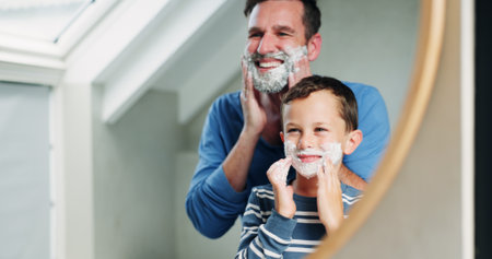 Shaving cream, reflection and dad with son in bathroom, happy and playful practice for growth or development. Father, boy and mirror in home for learning facial care, grooming and bonding with love.の写真素材