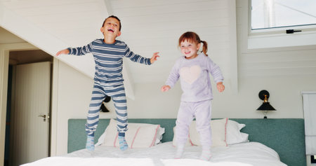 Children, jump and playing on bed in home for fun activity, entertainment and energy in morning with smile. Sibling love, people and playful with bonding, excited and freedom in bedroom on weekendの写真素材