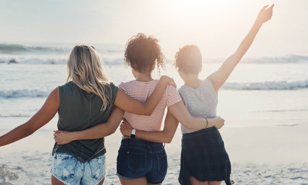 Women friends, back and hug at beach for summer vacation, adventure together and university break. Female people, group and embrace by ocean with freedom for travel, support and holiday trip in Miamiの写真素材