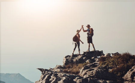 Hiking, high five and couple on mountain cliff with backpack for adventure, trekking and fitness. Travel, nature and happy people for wellness and exercise achievement on holiday, mockup or vacationの写真素材