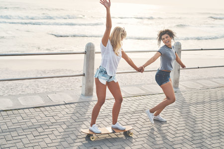 Beach, women and friends with skateboard, holding hands and summer holiday with fun, playful and...