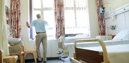 Back, senior man and hospital with depression, stress, sad and medical aid debt for elderly care. Male person, mental health and wellness in clinic for cancer treatment, appointment and consultationの写真素材