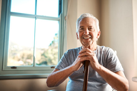 Portrait, walking stick and senior man in home with happiness for healthcare, support or wellness. Cane, medical and elderly person with disability in nursing facility for arthritis at house.の写真素材