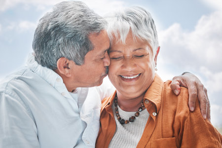 Elderly couple, kiss and hug in nature for love, romance and celebrating milestone with travel. Senior people, marriage and affection outdoor for healthy relationship, commitment and trust in supportの写真素材