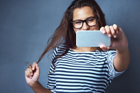 Woman, glasses and selfie with playful, optometry and confidence on gray studio background. Female person, memory and happy for eyewear, social media and smile with post, clear vision and eye careの写真素材