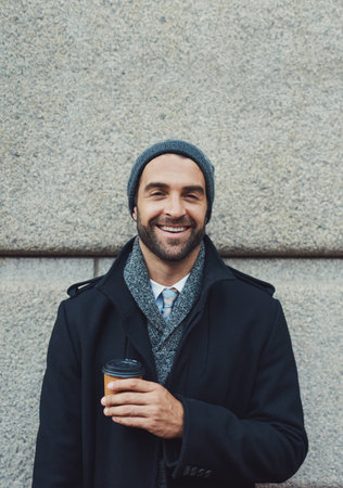 Fashion, portrait and happy man on wall with coffee in city on building background. Face, takeaway or person with drink outdoor on work commute, laugh or travel with trendy winter jacket in New Yorkの写真素材