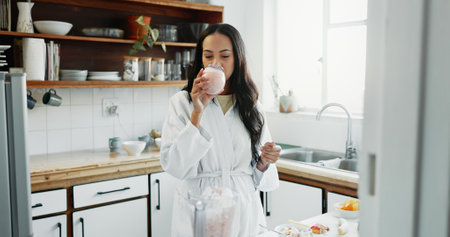 Woman, breakfast and drinking a smoothie in kitchen for vitamin nutrition, morning routine or healthy protein shake. Blender, person and organic detox for weight loss, vegan drink or wellness in homeの写真素材