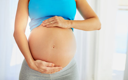 Pregnant, stomach and hands of woman in home by window for comforting, bonding and support in...