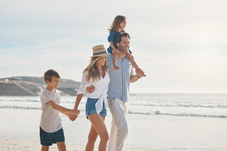Family, walking and holding hands on beach for travel, holiday and bonding together in summer on sand. Woman, dad and children by ocean for trip, vacation and support with happiness and carryingの写真素材