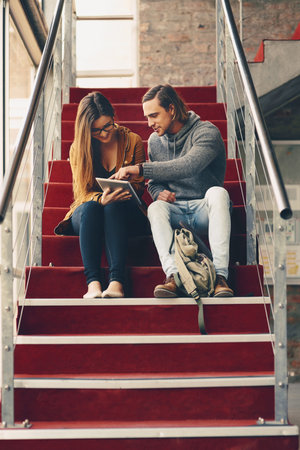 Tablet, couple and happy students learning on stairs to study course, info and education. Technology, man and woman in college on steps at university to prepare for exam, test or help with researchの写真素材