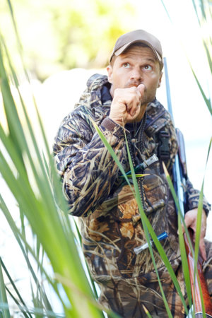 Man, hunter and duck whistle outdoor for camouflage, hunting wildlife and adventure activity of bird calling. Male person, gun and safety with gear, animal sound and birdwatching process of targetの写真素材