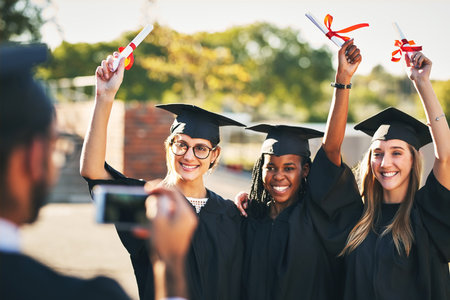 Phone, students and outdoor graduation photography, diploma celebration and capture memory. People, friends and certified together for university success, social media post and women for victoryの写真素材