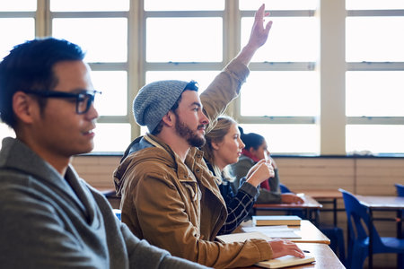 University, raised hand and man student with classmates in lecture for question, knowledge or learning. Scholarship, education and male person with group for college exam, test or assignment tutoringの写真素材
