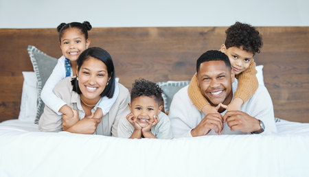 Parents, children and lying on bed for portrait with piggy back, care and bonding with love in family home. Kids, father and mother with smile, connection and relax with pride at apartment in Mexicoの写真素材