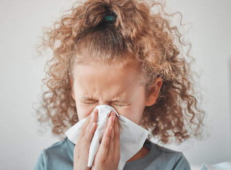 Sick, child and blowing nose with tissue in bedroom for hay fever, allergy or virus at home. Little girl, toilet paper and kid has medical problem at house for viral infection, bacteria or congestionの写真素材
