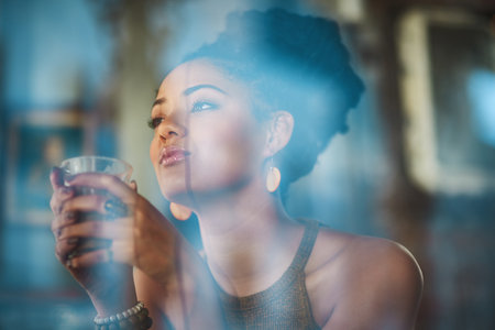 Woman, thinking and window with drink at coffee shop for morning, breakfast or beverage. Young female person, gen z or customer with cappuccino in wonder or thought for future dream at restaurantの写真素材
