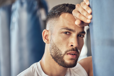 Exhausted man, portrait and boxer with punching bag for self defense training, practice or martial arts at gym. Tired male person or fighter in fitness for break after intense exercise or boxingの写真素材
