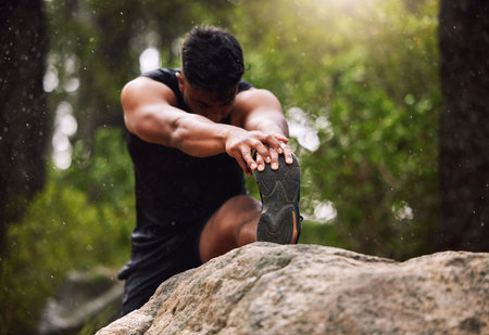 Leg, exercise and man stretching in forest with fitness workout, health and warm up in morning. Athlete, male person and flexibility in nature with muscle training, routine and preparation for runの写真素材