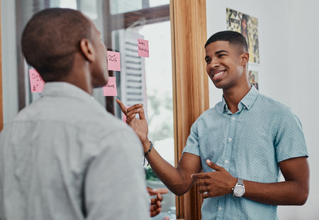 Office, meeting and glass wall for presentation, planning and sticky notes with statistics for report. African men, smile and small business, teamwork and collaboration for partnership or b2b projectの写真素材