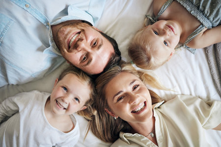 Portrait, happy and children with parents on bed for bonding, security and having fun together. Relax, home and girl kids laying with mom and dad for resting in bedroom at house in London from above.の写真素材