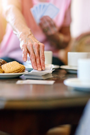 Elderly woman, table and hand with cards in retirement home for activity, hobby and fun on weekend. Games, senior person and relax with snack in living room for problem solving, strategy and contestの写真素材