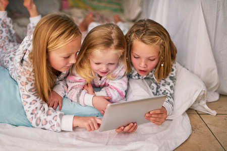 Girl, relax and kids with tablet in bedroom for online movie, streaming and watching cartoon show. Happy, sisters and smile with technology at home for bedtime, entertainment and bonding togetherの写真素材