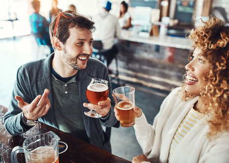 Date, couple and restaurant with drink, fun discussion and happy from romance and talk together. Pub, smile and people with conversation, love and bonding with beer and alcohol at bar for anniversaryの写真素材