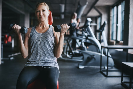 Weights, earphones and mature woman in gym for workout, training and exercise for mobility. Fitness,...