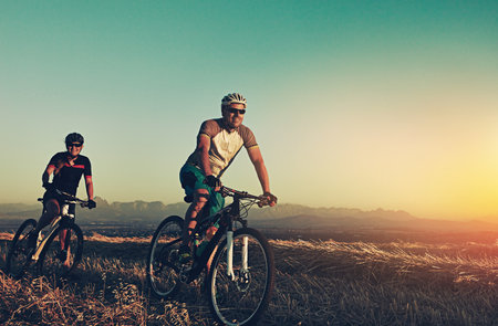 Sunset, mountain and people in bicycle race with helmet, exercise and adventure trail in nature together. Cycling, fitness and friends on bike in evening for outdoor workout, health and wellnessの写真素材