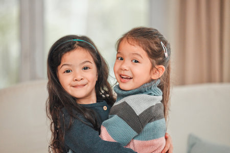 Portrait hug, girl kids and siblings in living room for love with bonding, connection and growth in home. Youth, Asian children and sister embrace for support, care and development in Singaporeの写真素材