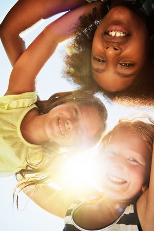 Happy, low angle and portrait of children with sunshine for friendship, playing and fun on camp. Diversity, youth and girls huddle for childhood, game and hug for school, recess and playgroundの写真素材