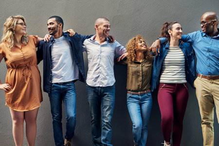 Happy business people, diversity and team with hug for company growth together on a wall background. Group of diverse, young employees and smile in row or line for unity, creative startup or about usの写真素材