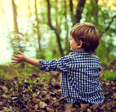 Boy, forest and playing with bubbles in nature for fun, games and happy on earth day or climate change in future. Back of child or kid relax in woods with childhood, growth and outdoor developmentの写真素材
