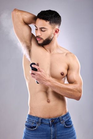 Body, man and spray with deodorant on armpit in studio for hygiene, fragrance and wellness. Scent, shirtless and male person by white background for grooming, cleaning and perfume for fresh smellの写真素材