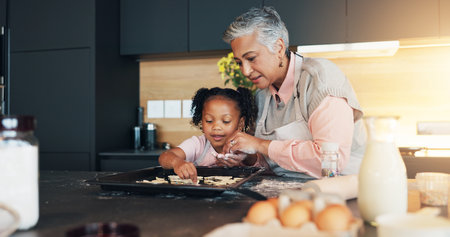 Baking, child and grandmother helping with cookies for decoration, learning and childhood development. How to, baker woman and girl bonding in kitchen with teaching cake recipe, support and educationの写真素材
