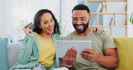 Happy couple, sofa and tablet with credit card for ecommerce, payment or banking app at home. Excited man, woman or shoppers with smile on technology for online shopping, transaction or purchaseの写真素材