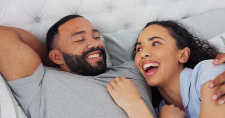 Bed, cuddle and couple with laugh for bonding, comfortable and connection in relationship at home. Happy people, man and woman with love embrace for joke, commitment and affection with hug in houseの写真素材